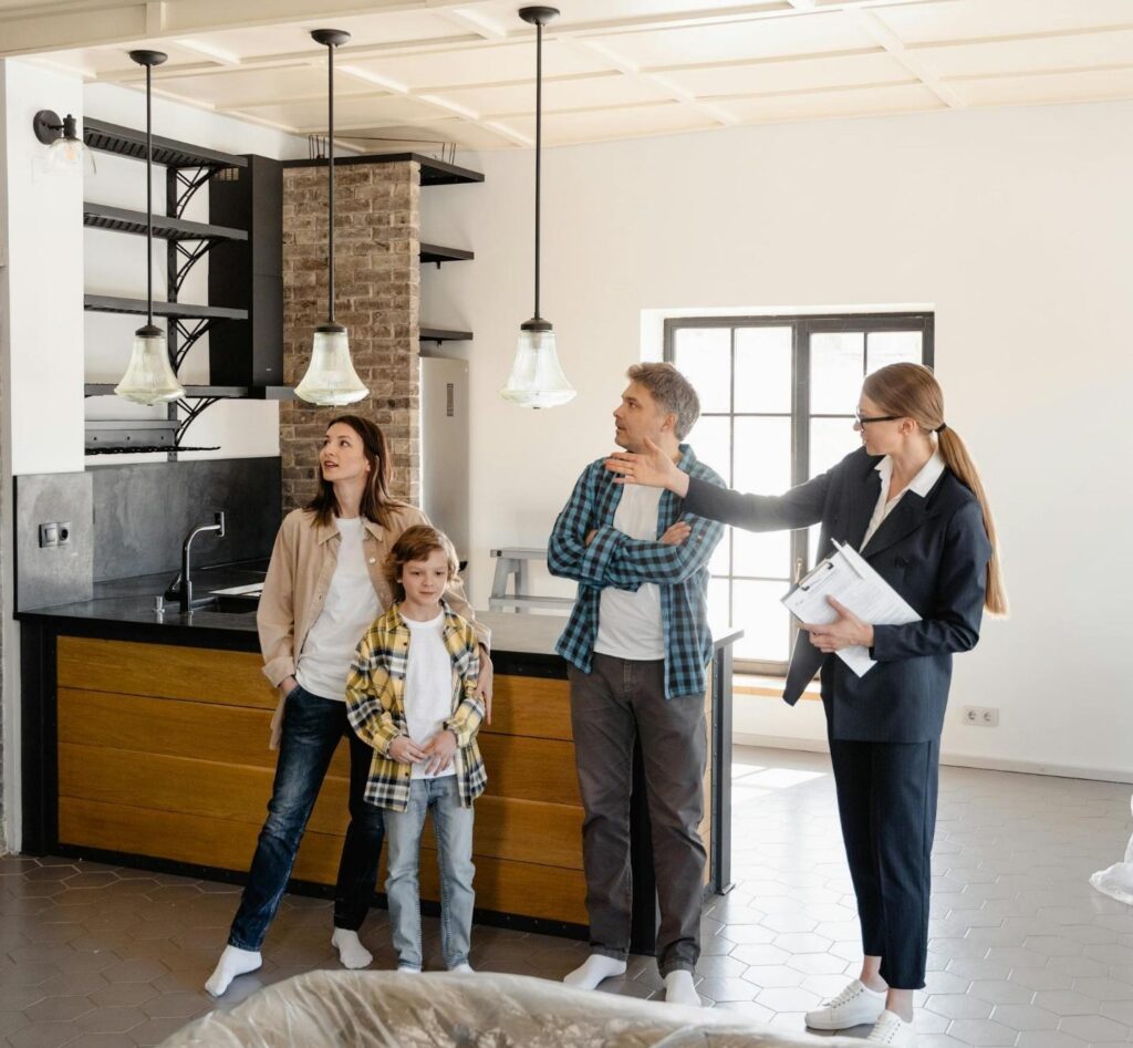 Real estate agent giving a tour of a modern kitchen to a family, explaining the features and benefits to the parents and their child. The agent is pointing to the lights and engaging with the clients, demonstrating a professional and informative approach to building relationships with homeowners and developers.